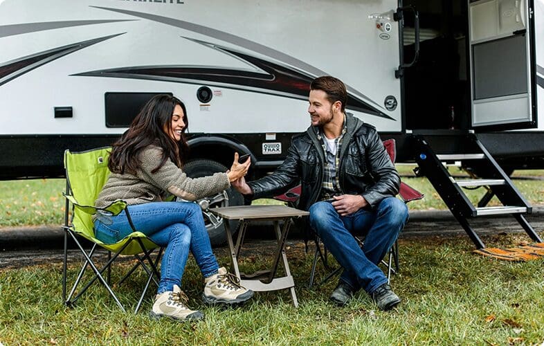 A man and woman sitting at a table outside of an rv.