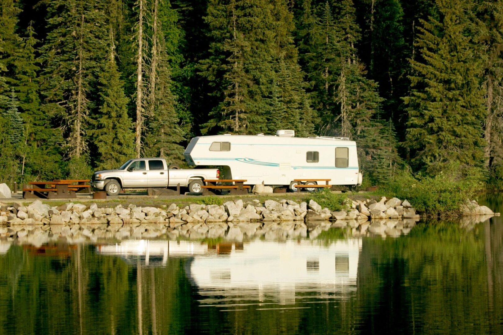 A truck and camper are parked on the shore of a lake.